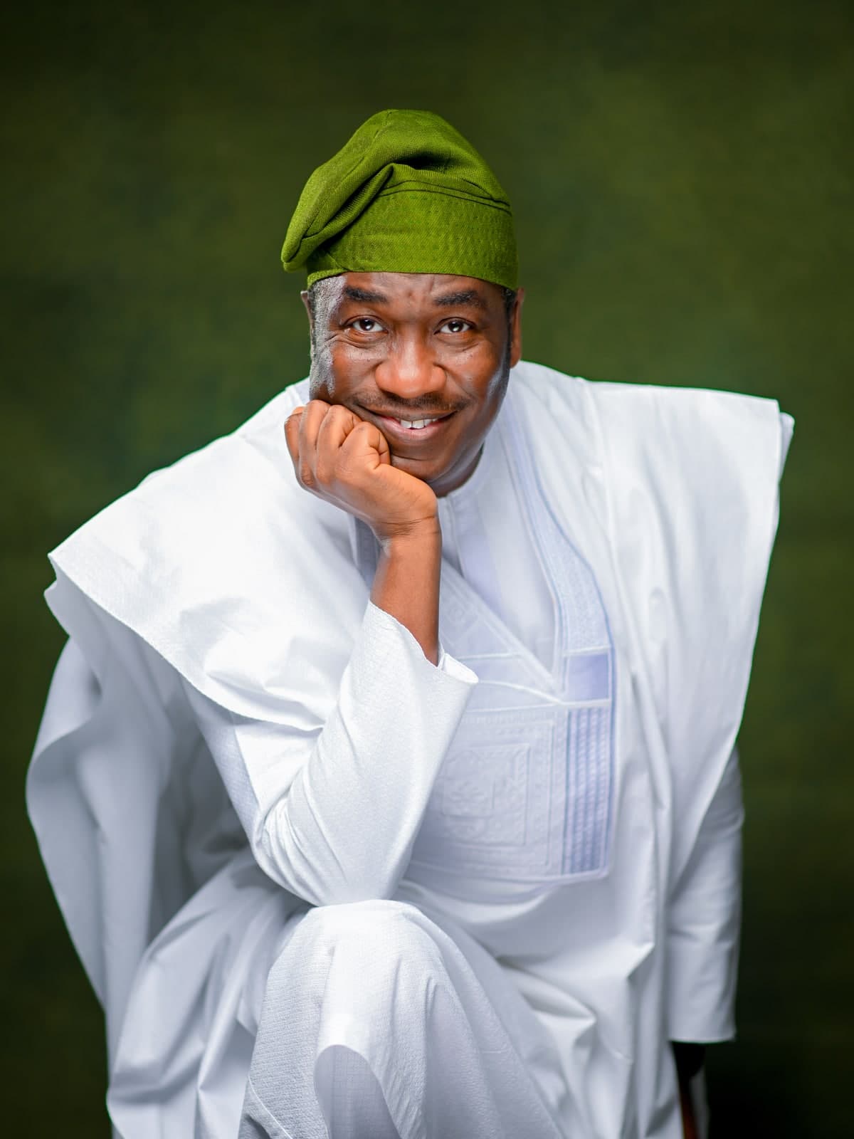 Dr. Kadri Obafemi Hamzat, close portrait in a white agbada and green cap, hand resting at his chin, against a dark green backdrop.