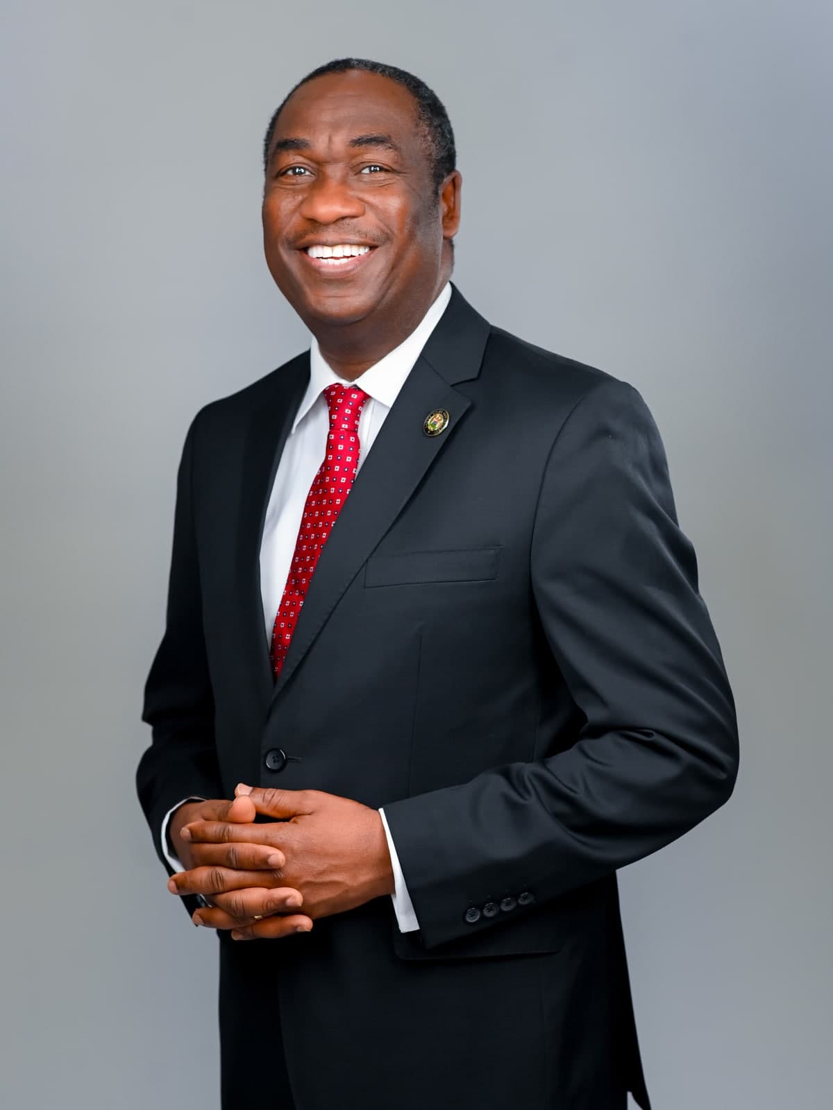 Dr. Kadri Obafemi Hamzat, standing with hands clasped, turned slightly to one side, in a dark suit and red tie.