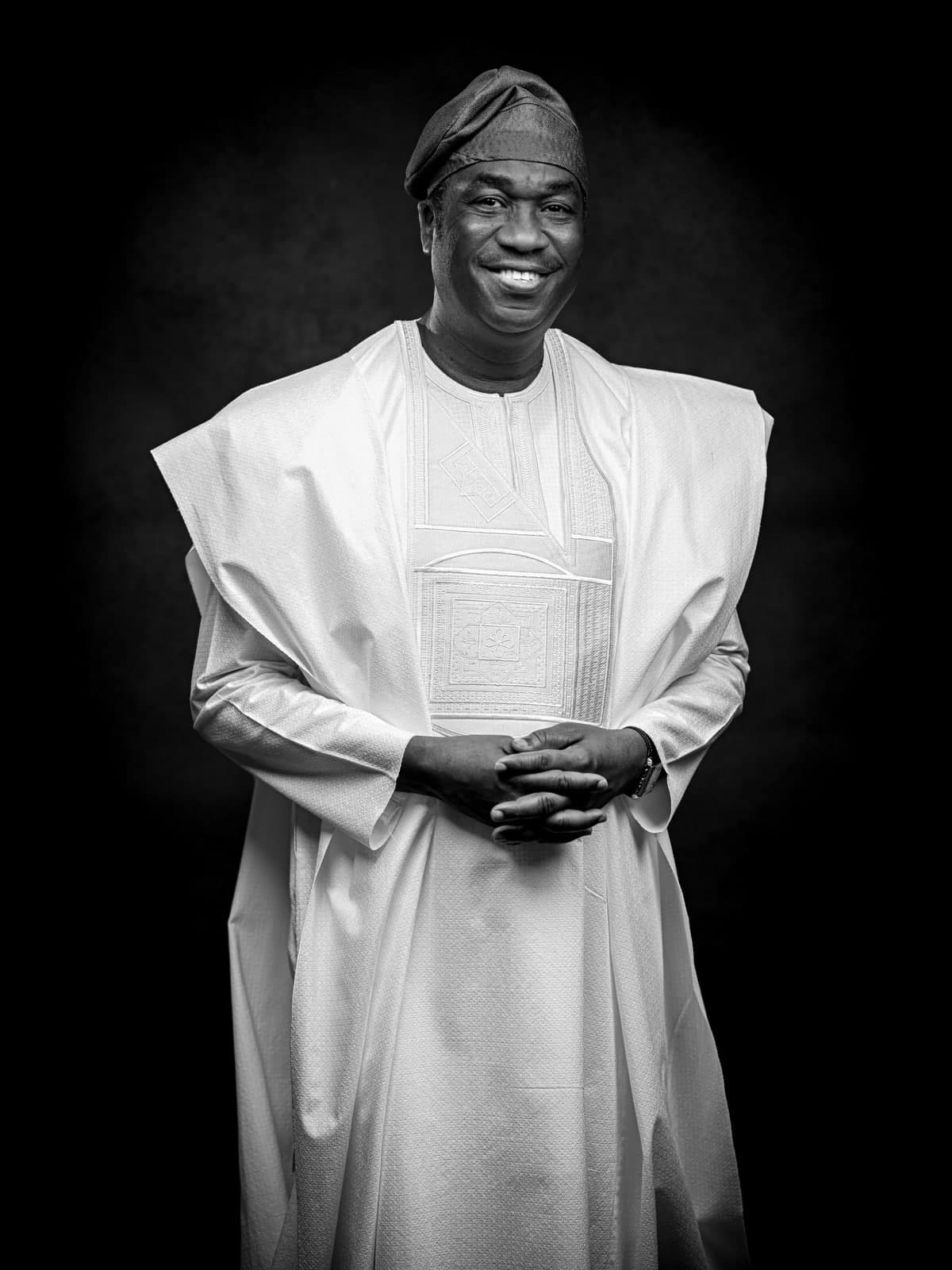 Dr. Kadri Obafemi Hamzat, a black and white portrait standing with hands clasped, in a white agbada and cap.