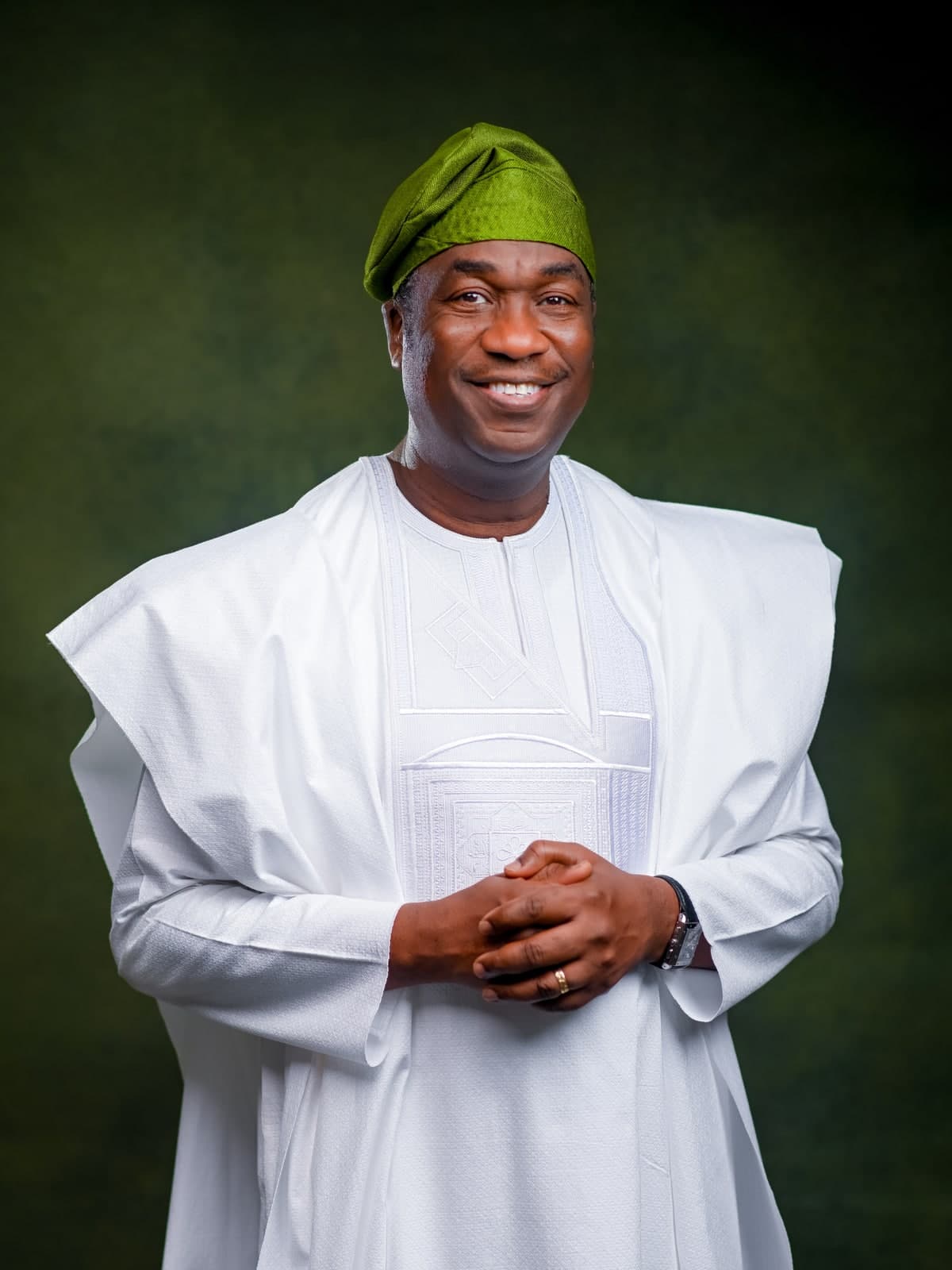 Dr. Kadri Obafemi Hamzat, standing with hands clasped, in a white agbada and green cap, against a green backdrop.