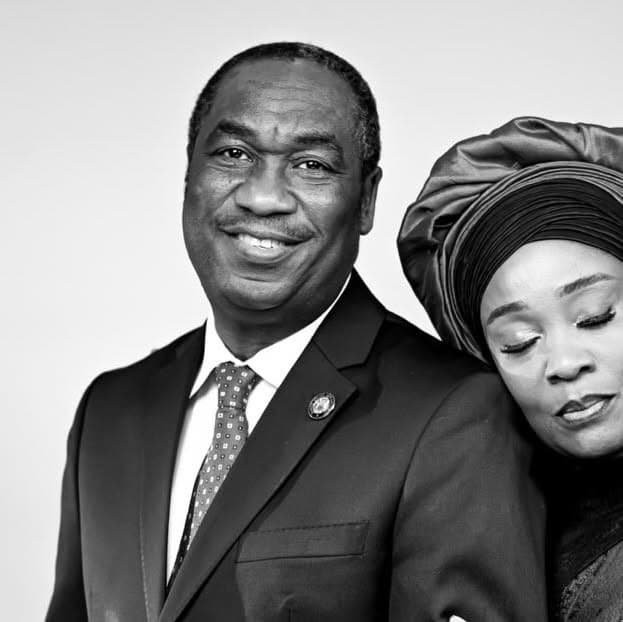 Black-and-white photograph of Dr. Kadri Obafemi Hamzat, smiling, in a dark suit, white shirt and patterned tie, with his wife, Mrs. Oluremi Hamzat, in a gele, her eyes closed and her head resting on his shoulder.